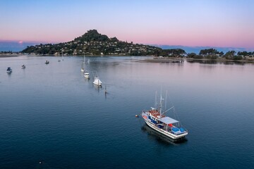 Fototapeta premium Tranquil morning scene on the water. Fishing boat navigates calm waters near coastal town. Peaceful harbor at dawn. Tairua, Coromandel Peninsula, New Zealand