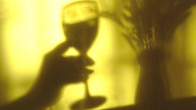 Blurred shadow on shabby yellow wall. Hand of someone holding wine glass. Atmospheric evening mood