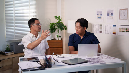 Engineers brainstorming construction ideas while referencing blueprints and material lists at the desk