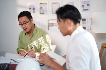 Engineers collaborating on project details with blueprints, material samples, and technical...