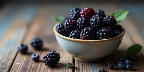 A rustic bowl brimming with plump, dark blackberries and a scattering of blueberries rests on a weathered wooden surface, capturing the essence of a simple yet delightful harvest