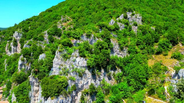 Enchanting aerial pan left push-in shot from Pioraco, showing the rocky surface of the Sibillini Mountains filled with greenery, seguing into the Potenza river valley with pastures, road, cars, houses