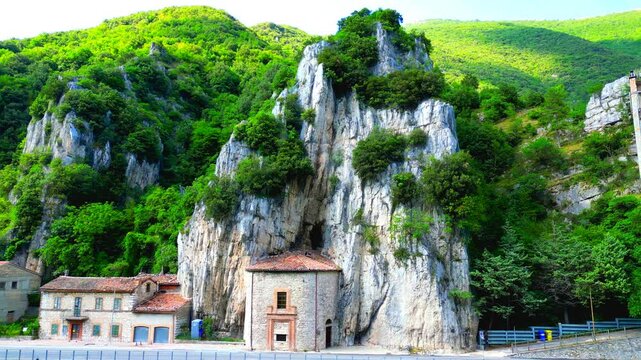 Stupendous aerial truck left pan left shot from Pioraco, a vision ranging from the Eremo della Madonna della Grotta inside the rocky green-topped Sibillini Mountains, to the Potenza River green swath
