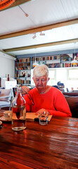 An elderly woman is enthusiastically reading a book in a cafe.