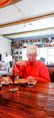 An elderly woman is enthusiastically reading a book in a cafe.