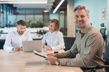 Businessman with his staff, people group in background at modern bright office indoors.