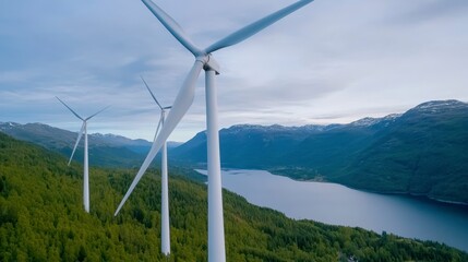 Aerial view of wind turbines on a green mountainside overlooking a serene lake under a partly cloudy sky. The scene depicts clean energy production