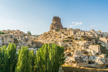 Fototapeta premium Panoramic view of Uchisar Castle rock fortress and ancient cave village with green trees in Cappadocia, Turkey