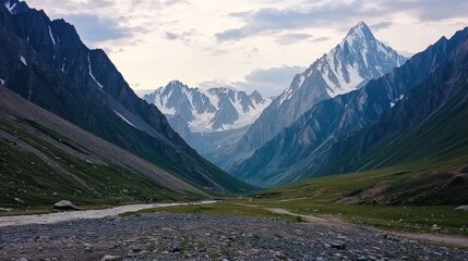 Mountain valley vista, rocky path, snow-capped peaks, cloudy sky