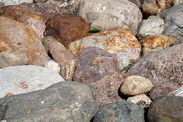 Small boulders close-up. Large pebbles of different colors and green grass growing between the stones. Oval-shaped stones are scattered randomly on the grass.