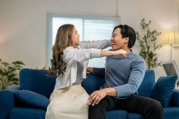 Fototapeta premium A man and a woman are sitting on a blue couch, laughing and hugging each other
