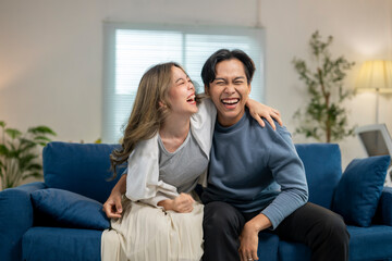Obraz premium A man and a woman are sitting on a blue couch, laughing and hugging each other