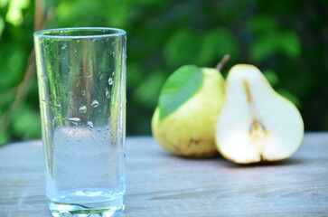 Pear juice on wooden table outdoors. Glass of juice and pears fruits, summer garden on background. Healthy summer drinks concept.