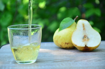 Pear juice on wooden table outdoors. Glass of juice and pears fruits, summer garden on background. Healthy summer drinks concept.