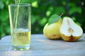 Pear juice on wooden table outdoors. Glass of juice and pears fruits, summer garden on background. Healthy summer drinks concept.