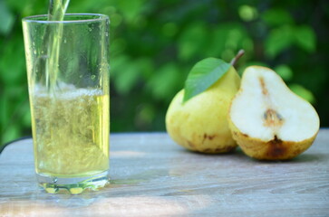 Pear juice on wooden table outdoors. Glass of juice and pears fruits, summer garden on background. Healthy summer drinks concept.