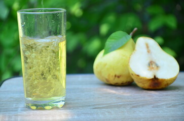 Pear juice on wooden table outdoors. Glass of juice and pears fruits, summer garden on background. Healthy summer drinks concept.