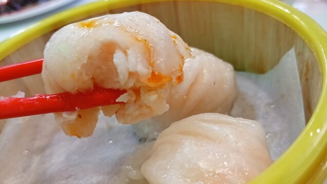 close up image of picking up hakau or steamed shrimp dumplings with chopsticks