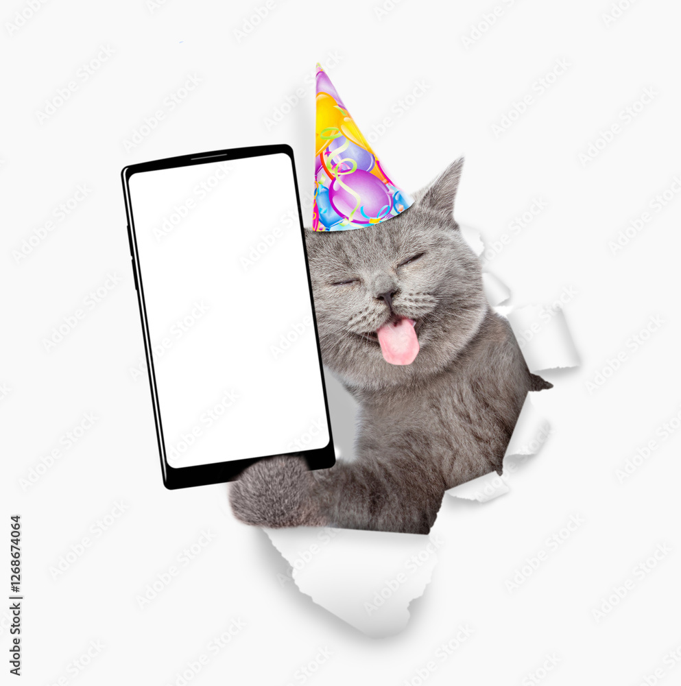 Poster happy cat with tongue out wearing party cap showing smartphone with white blank screen in it paw thr