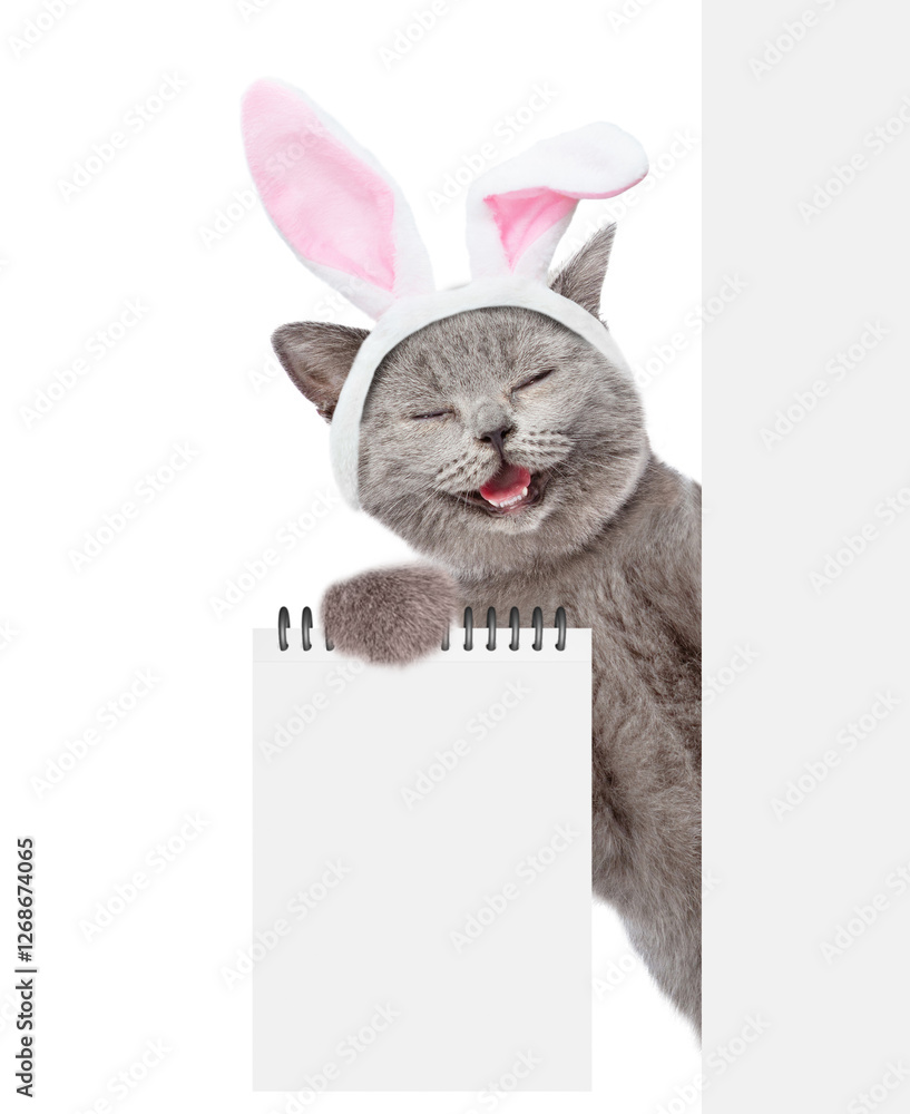 Aufkleber Happy cat wearing easter rabbits ears looks from behind blank white banner and shows blank notepad. Empty space for text. Isolated on white background