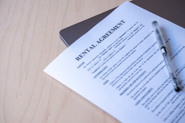 Rental Agreement Contract on Space Grey Laptop with Pen on Wooden Background