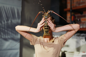Woman holding lobster up to face while covering eyes with hands in playful and humorous act