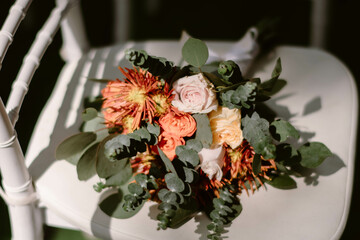 A flower bouquet composed of white, pink, and orange roses, placed on a white chair, with light and shadows
