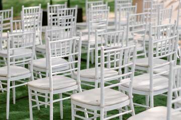 Many white chairs are neatly arranged in an orderly manner to be used in a wedding ceremony held on the grassy field in the garden