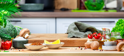 Healthy eating, cooking, food blogging background. Oak cutting board with vegetables, herbs, mushrooms and linen towel on cozy kitchen with wooden table, kitchenware and ingredients