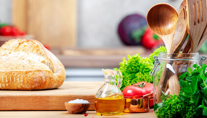 Healthy eating, cooking, food blogging background. Oak cutting board with bread, herbs, vegetables on cozy kitchen with wooden table, kitchenware and utensils