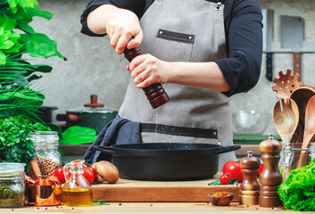 Chef grinds salt in spice grinder over cast iron skillet. Cozy kitchen with wooden table,...