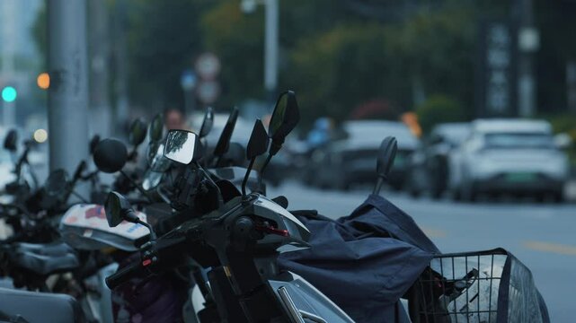 Parked mopeds in a row on the street during the day, close view of the scooters handlebars and mirrors.
