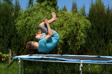 A young boy joyfully performing an impressive flip on a trampoline beneath clear blue skies