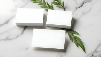 Dos tarjetas de presentación blancas sobre una mesa de mármol con una maqueta de rama verde