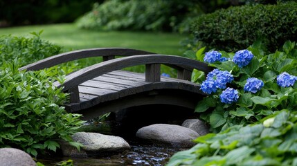 A wooden bridge arches over a small stream, surrounded by lush greenery and vibrant blue hydrangeas.