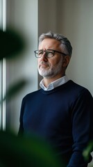 Fototapeta premium Middle-aged man gazing thoughtfully out of a window in a minimalist setting during daylight hours