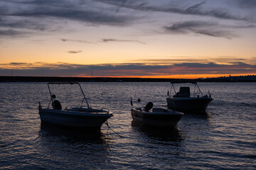 Naklejka premium Boats silhouetted sunrise sky background. Peaceful sunrise scene with fishing boats anchored in the harbor on calm sea. Golden horizon, early morning at bay