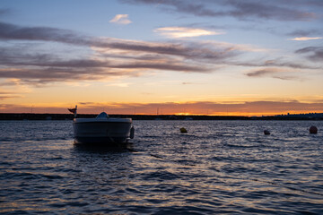 Golden sunrise over quiet harbor with lone boat on calm sea. Peaceful sunrise scene with fishing...
