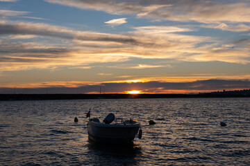 Golden sunrise over quiet harbor with lone boat on calm sea. Peaceful sunrise scene with fishing boat anchored in harbor on waters and gentle waves. Beautiful golden horizon, early morning at bay