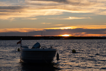 Golden sunrise over quiet harbor with lone boat on calm sea. Peaceful sunrise scene with fishing boat anchored in harbor on waters and gentle waves. Beautiful golden horizon, early morning at bay