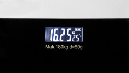 A sleek digital weighing scale with a black surface and an illuminated display showing "kg" and ambient temperature.