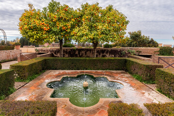 Beautiful decorative fountain next to orange trees in the gardens of the Generalife in the Alhambra, Granada, Andalusia.