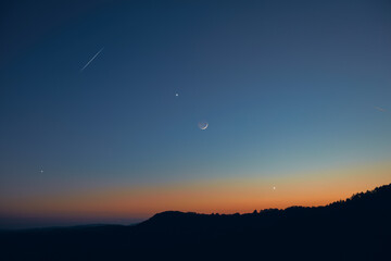 Countryside silhouettes under the stars, meteor trail and crescent Moon.