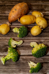 Top view of various potatoes, broccoli and sweet potato raw on a wooden table.