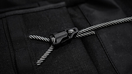 A detailed view of a black fabric backpack with a secure buckle and striped drawstring, showcasing...