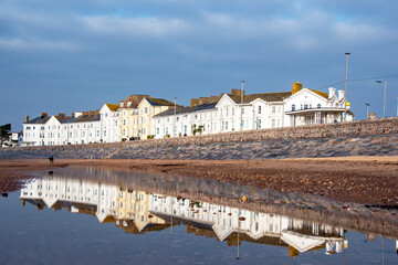 Obraz premium Seaside properties, homes and houses with a strong reflection in standing water on a beach. Seafront scene and lifestyle picture. Retirement homes and coastal living. Estate agent.