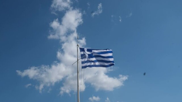 Worn Greek flag close up, waving against clear blue sky, symbolizing resilience