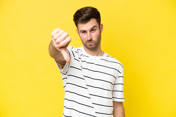 Young caucasian man isolated on yellow background showing thumb down with negative expression