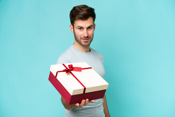 Young caucasian man holding a gift isolated on blue background with happy expression