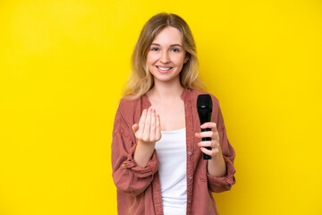 Young singer caucasian woman picking up a microphone isolated on yellow background inviting to come...